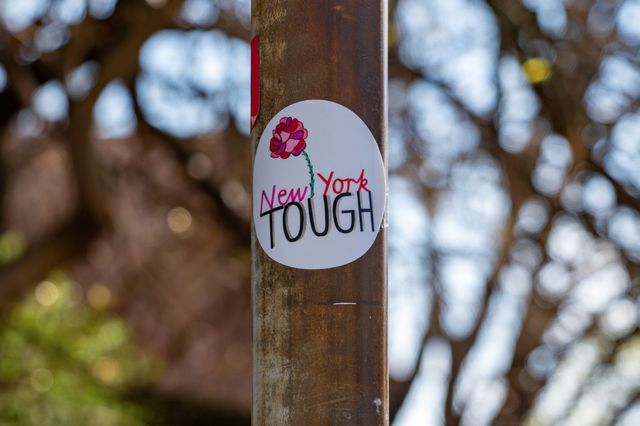 A photo of a sticker on a lamppost reading "new york tough"